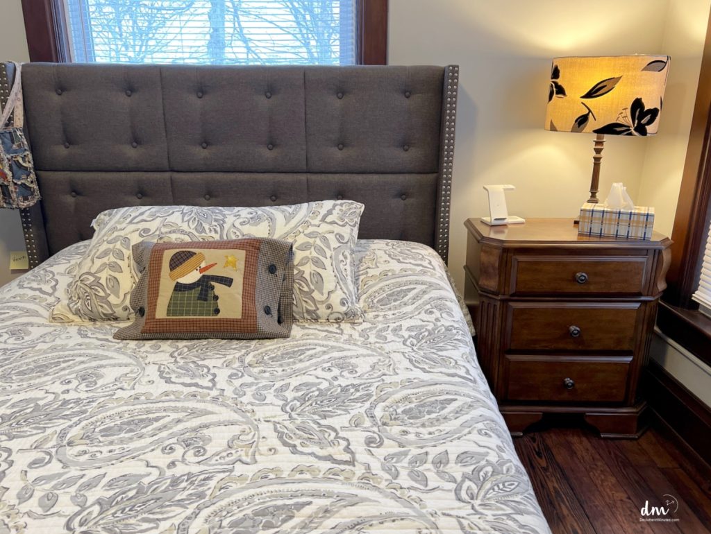 a grey bed with a snowman pillow next to a neat and organized night stand
